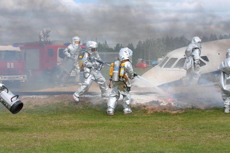 Сотрудники МЧС в специальных защитных костюмах тушат пожар у упавшего самолета